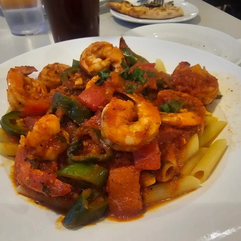 A white plate of Luberto's shrimp and penne pasta with red sauce and colorful bell peppers.