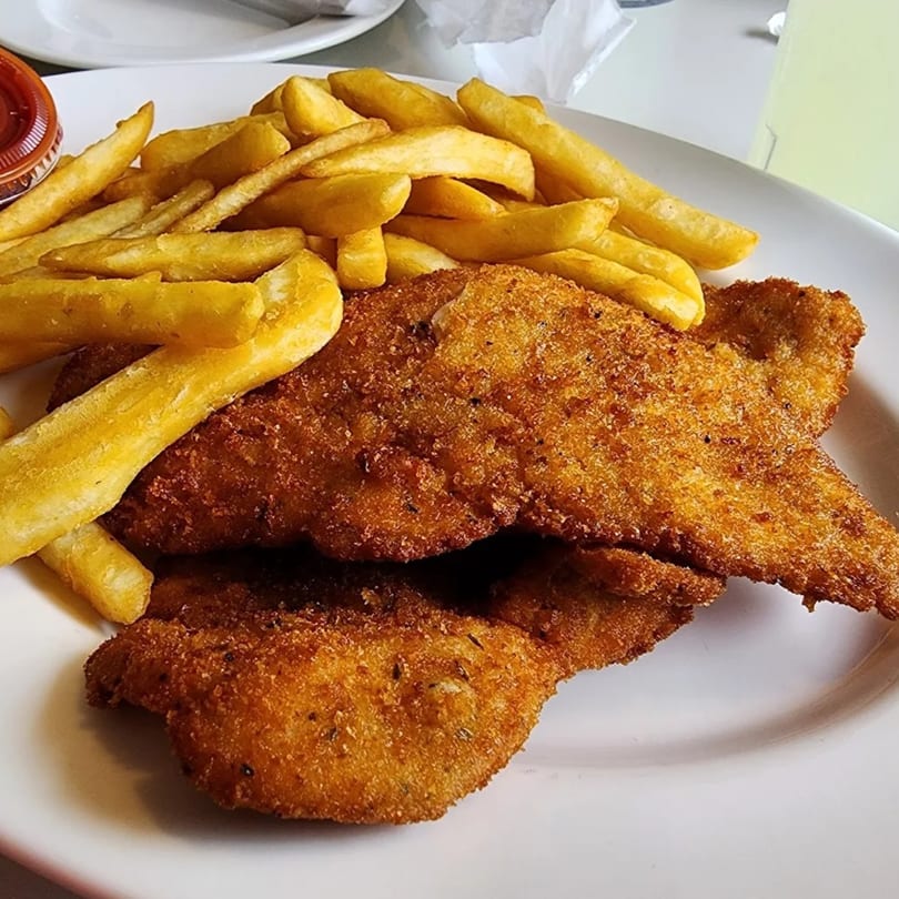 Golden-brown fried chicken cutlets and a pile of thick-cut french fries on a white plate.