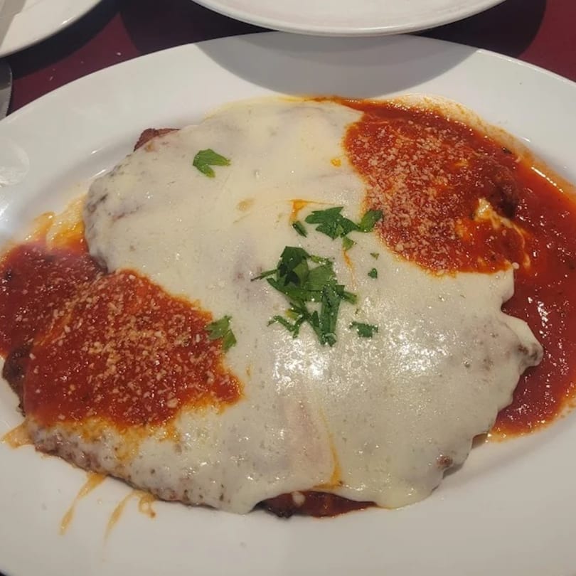 Luberto's chicken parmesan with melted mozzarella, red sauce, grated cheese, and parsley on a white plate.