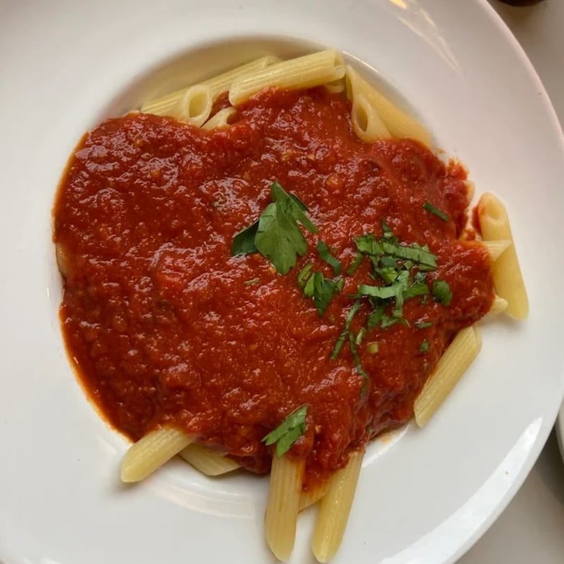 Penne pasta with rich red marinara sauce and fresh green herbs on a white plate.