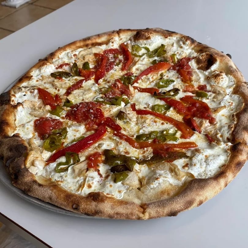 Luberto's Brick Oven Pizza with white sauce, red peppers, and green peppers on a white table.