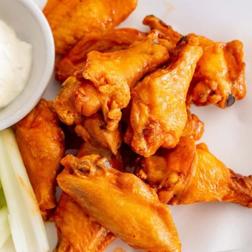 Close-up of golden-brown chicken wings with a side of ranch dressing and celery sticks.