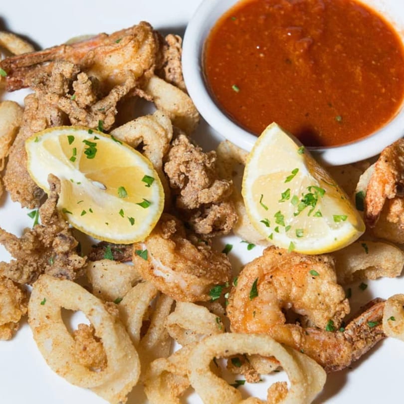 Crispy fried calamari and shrimp with lemon wedges and a side of red marinara sauce.